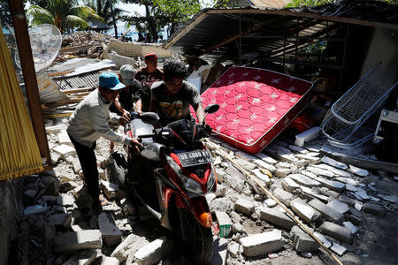 Villagers push a motorcycle along ruins after an earthquake hit Lombok island in Pamenang, Indonesia August 6, 2018. REUTERS/Beawiharta