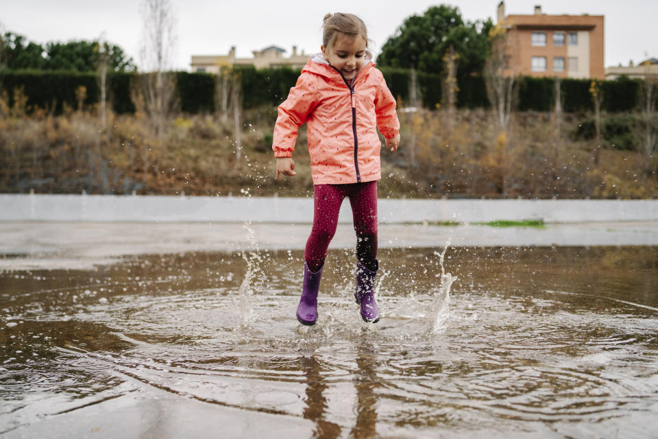 A girl in a raincoat is splashing in a puddle