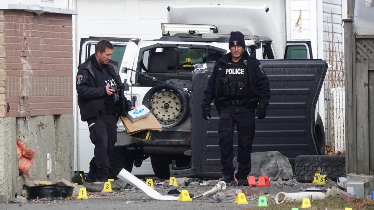 Kingston Police officers investigate the scene of the collision on Tuesday morning. Two houses were damaged in the incident and two suspects fled the scene, police said. (Dan Taekema/CBC - image credit)