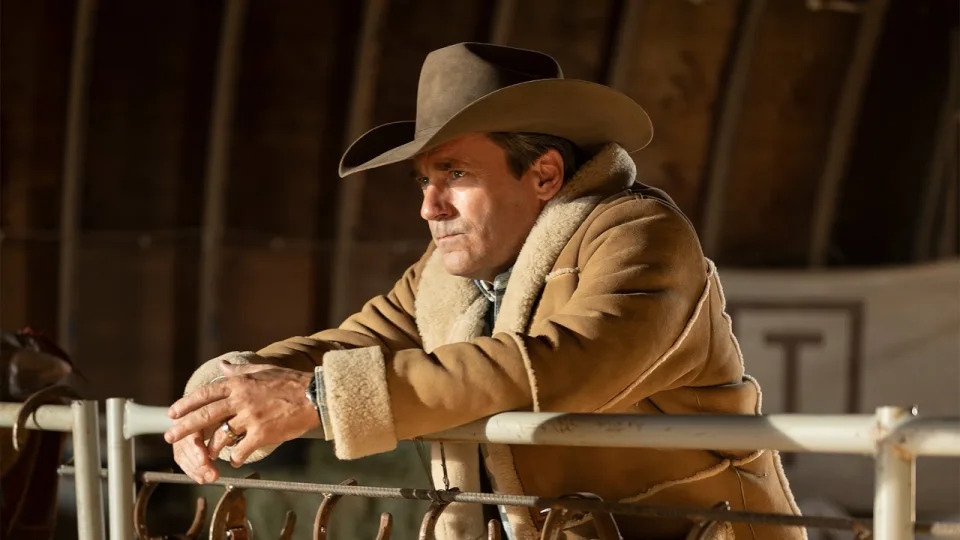 Jon Hamm in cowboy gear, leaning against a barn gate in Fargo.