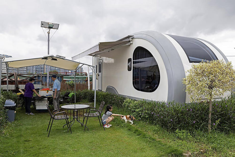 A couple cleans up the table outside the signature stargazing caravan of Park Nature, a glamping site that offers luxury caravans packages in Hong Kong on Aug. 14, 2021, while their granddaughter plays with a cat in Hong Kong. From the Great Wall to the picturesque Kashmir valley, Asia's tourist destinations are looking to domestic visitors to get them through the COVID-19 pandemic's second year. With international travel heavily restricted, foreign tourists can't enter many countries and locals can't get out. The difficulty of traveling abroad has made glamping, or glamourous camping, popular in Hong Kong. (AP Photo/Matthew Cheng)