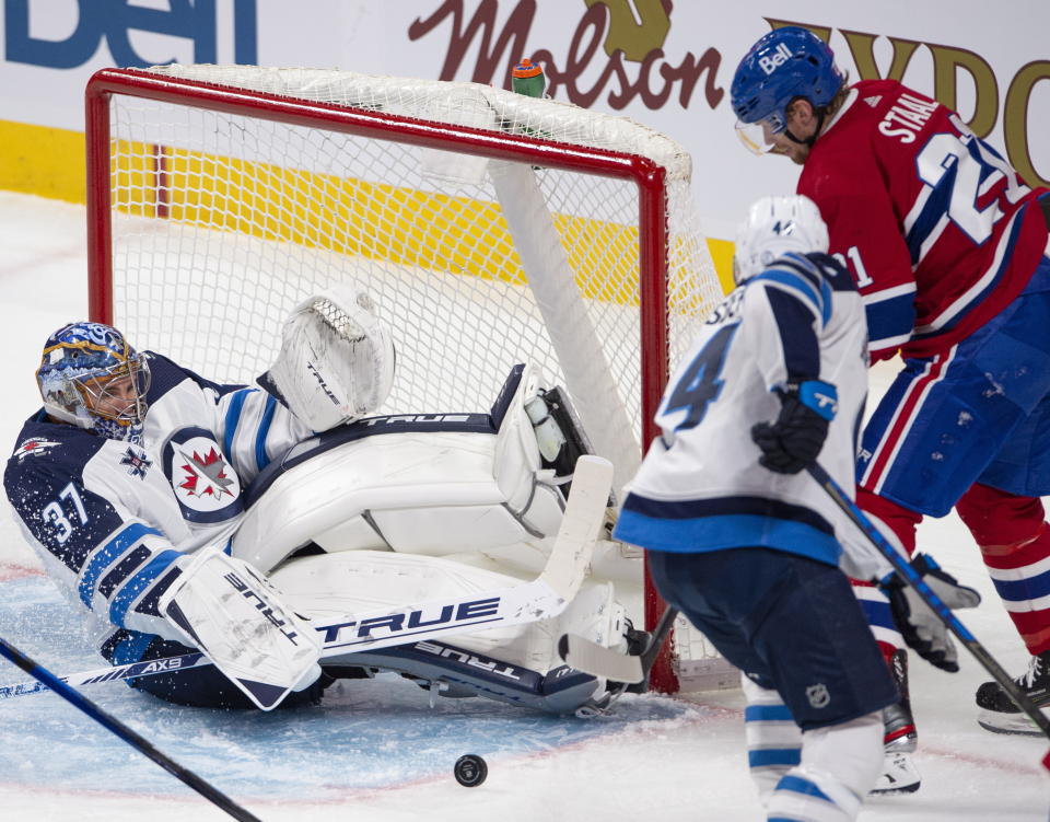 Winnipeg Jets goaltender Connor Hellebuyck (37) makes a save as Montreal Canadiens' Eric Stall and Jets' Josh Morrissey (44) look for the rebound during the second period of an NHL hockey game, Thursday, April 8, 2021 in Montreal. (Ryan Remiorz/The Canadian Press via AP)