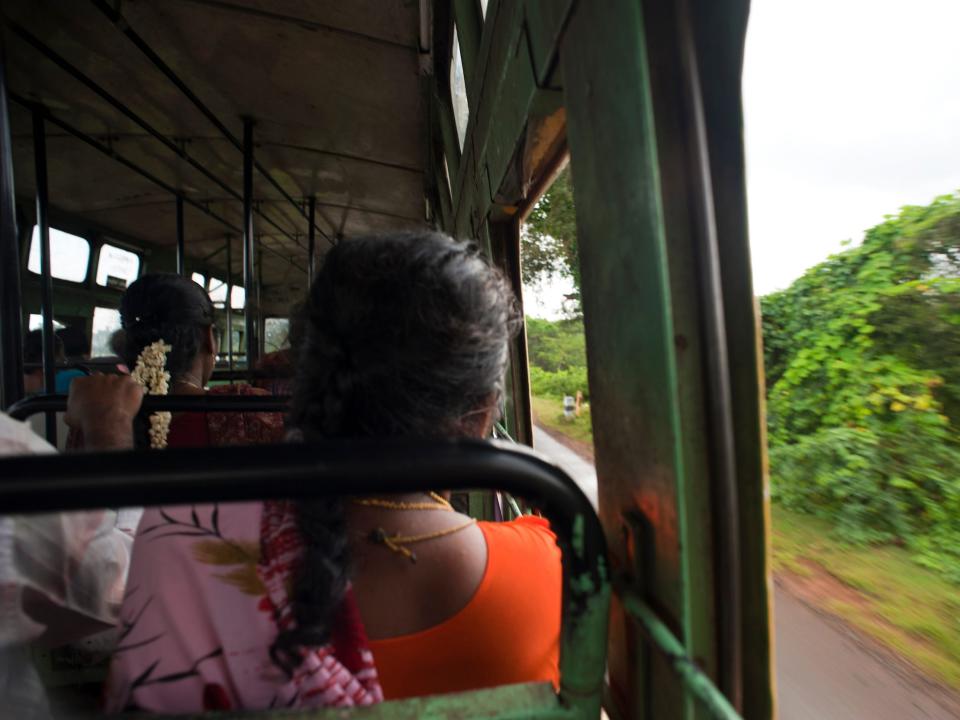 Passengers are seen inside a bus in Chettinad, India. A woman with her hair in a braid wearing a pink scarf and orange shirt is seated in the foreground.