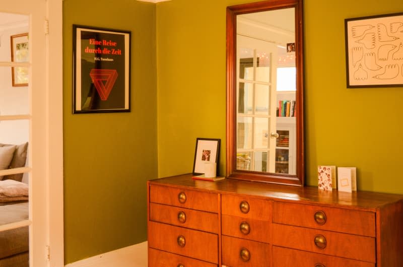 Green walled bedroom with framed art and mirrored dresser.