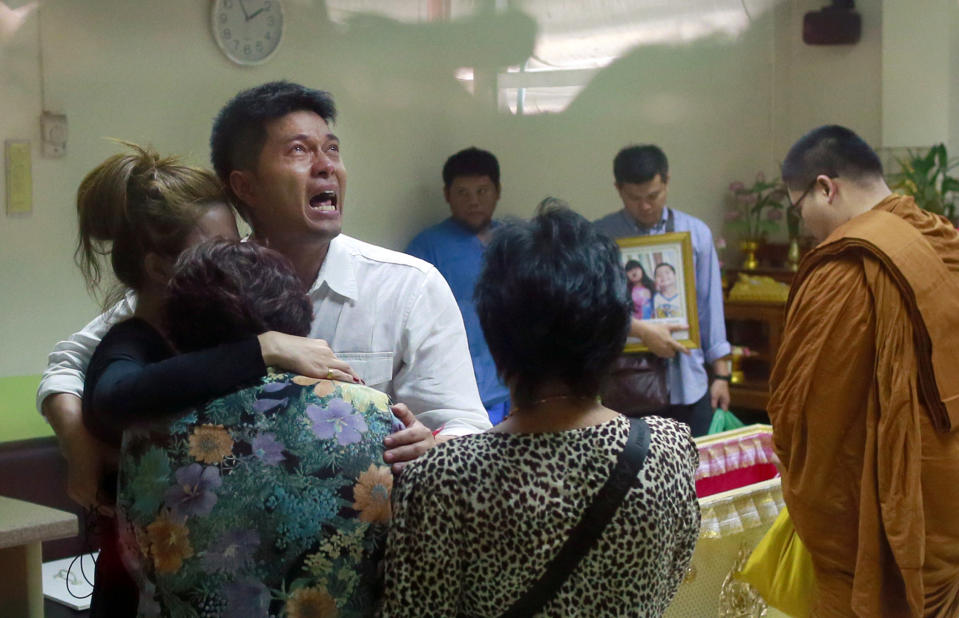 Tayakorn Yos-ubon, the father of two children killed in Sunday's bomb attack on an anti-government protest site, is embraced by his family as he breaks down during a ceremony at a hospital when he collects their bodies, Monday, Feb. 24, 2014, in Bangkok, Thailand. Two young siblings, 6-year-old girl Patcharakorn and her 4-year-old brother Korawit, along with another woman were killed in an apparent grenade attack against anti-government protesters occupying an upscale shopping area of Thailand's capital on Sunday, the latest violence in a months-long political crisis that is growing bloodier by the day. (AP Photo/Wason Wanichakorn)