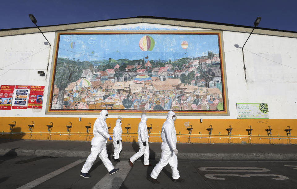 Workers in protective body suits walk past sinks for hand washing at the "Corabastos," one of Latin America's largest food distribution centers, as they work to disinfect it to help contain the spread of the new coronavirus in Bogota, Colombia, Friday, April 10, 2020. (AP Photo/Fernando Vergara)