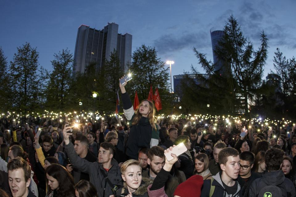 Demonstrators wave their cell phones as they gather in front of a new built fence blocked by police, during a protest against plans to construct a cathedral in a park in Yekaterinburg, Russia, Wednesday, May 15, 2019. Hundreds of riot police have surrounded a park in Russia's fourth-largest city before what's expected to be a third consecutive day of protests against building a new cathedral. (AP Photo/Anton Basanayev)