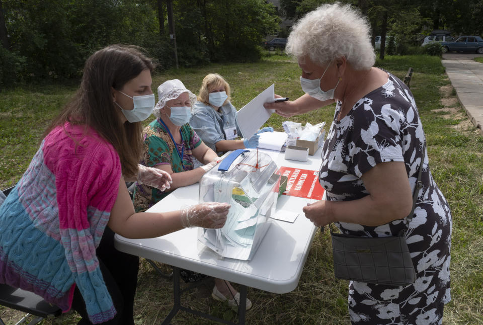 Members of the election commission wearing face masks to protect against coronavirus infection help to a voter to cast her ballot at an outdoor polling station in Naziya village, 80 km (50 miles) east of St.Petersburg, Russia, Sunday, June 28, 2020. Polls have opened in Russia for a week-long vote on a constitutional reform that may allow President Vladimir Putin to stay in power until 2036. (AP Photo/Dmitri Lovetsky)
