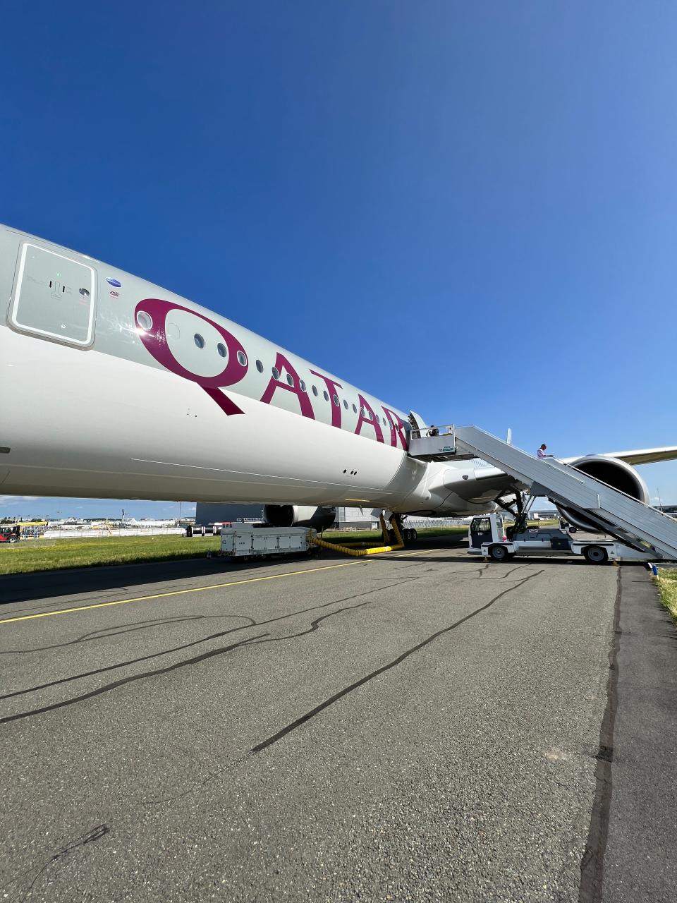 A wide-angle view shows the Qatar Airways logo on an Airbus A350 parked on the tarmac, and the stairs leading up to it.