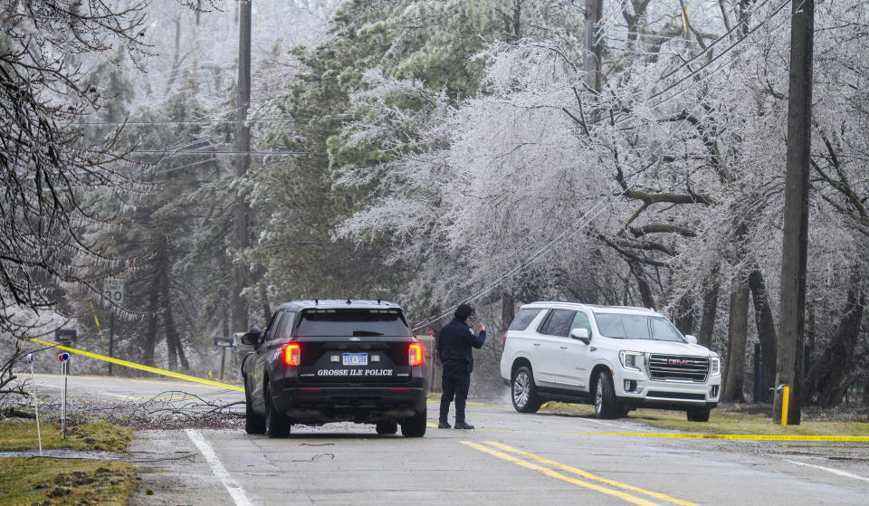 Officer Louis Hurtado of the Grosse Ile Police Department directs a car under a downed secondary power line on Parke Lane on Grosse Ile, Thursday, Feb. 23, 2023. (Andy Morrison/Detroit News via AP)