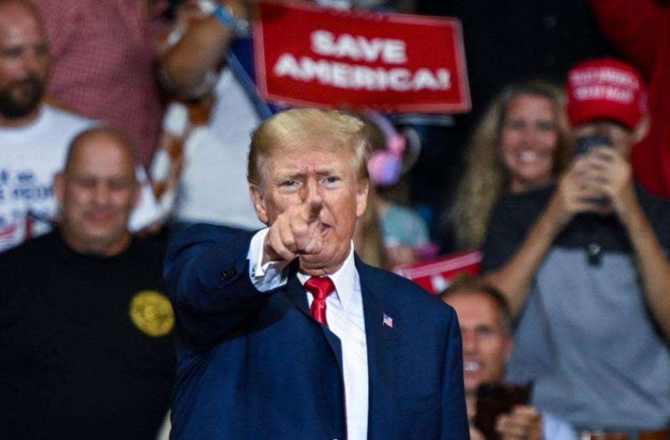 Donald Trump zeigt mit dem Finger in die Kamera, während die Unterstützer hinter ihm „Save America!“ halten.  Zeichen.