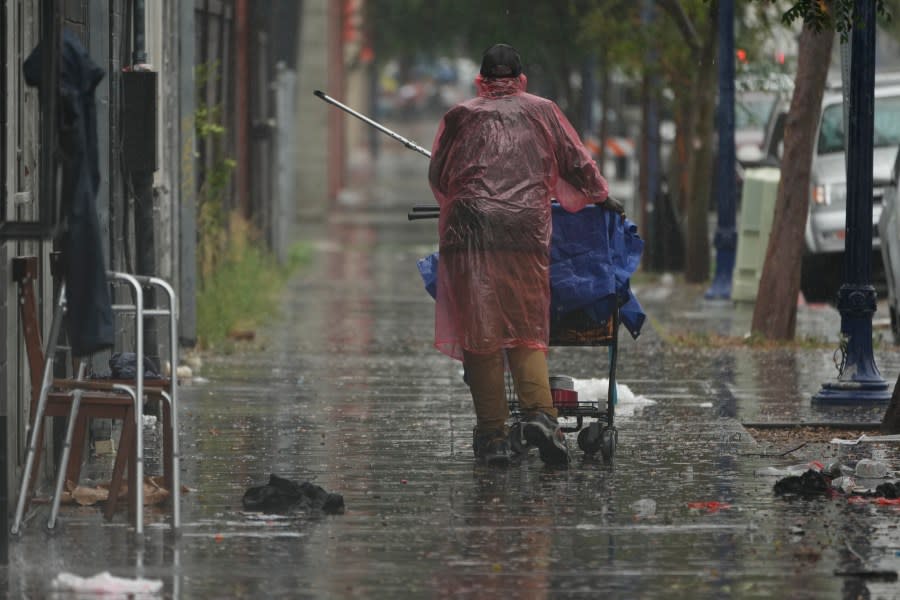 A homeless person walks under a light rain brought by Tropical Storm Hilary in downtown San Diego, Sunday, Aug. 20, 2023. (AP Photo/Damian Dovarganes)