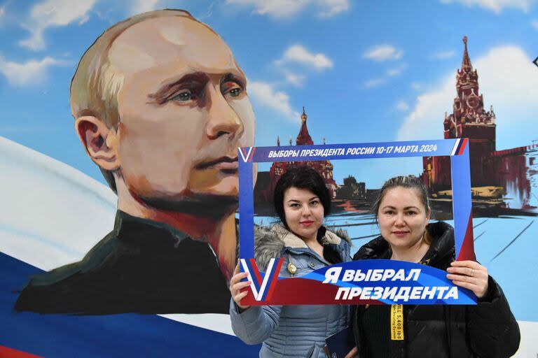 Mujeres posan frente a un mural que representa al presidente ruso Vladimir Putin después de votar en las elecciones presidenciales de Rusia en un colegio electoral de una escuela local en Donetsk, el 15 de marzo de 2024.