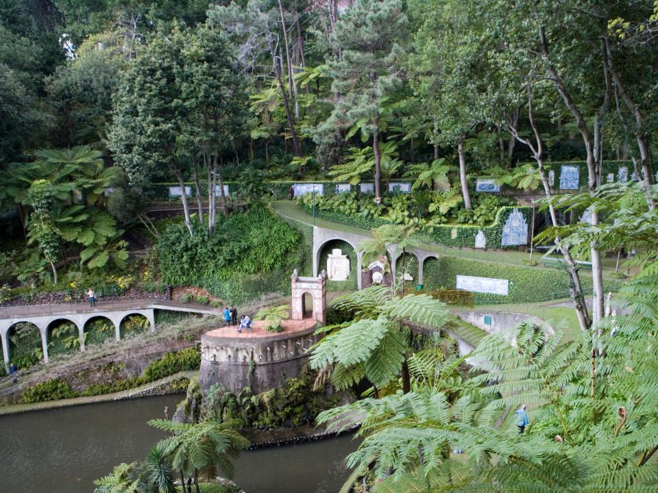 A greenery-filled botanical garden with pathways, and a body of water running through it.