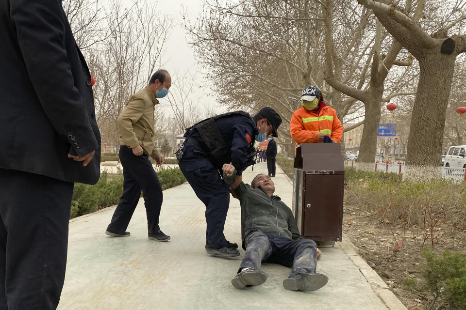 An officer helps up a drunk man passed out by a trash bin in Poksam County, in northwestern China's Xinjiang Uyghur Autonomous Region on March 21, 2021. Four years after Beijing's brutal crackdown on largely Muslim minorities native to Xinjiang, Chinese authorities are dialing back the region's high-tech police state and stepping up tourism. But even as a sense of normality returns, fear remains, hidden but pervasive. (AP Photo/Ng Han Guan)