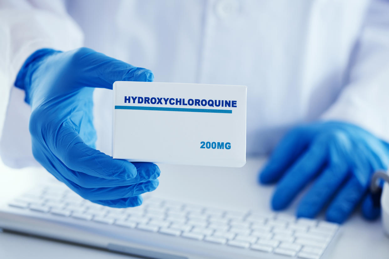 closeup of a man, wearing a white coat and blue surgical gloves, having a simulated box of hydroxychloroquine in his hands