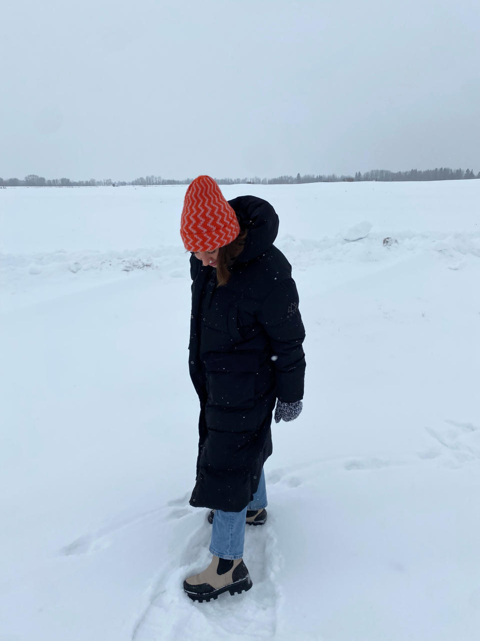 woman wearing red toque, black parka, blue jeans and cougar winter boots outside in snow