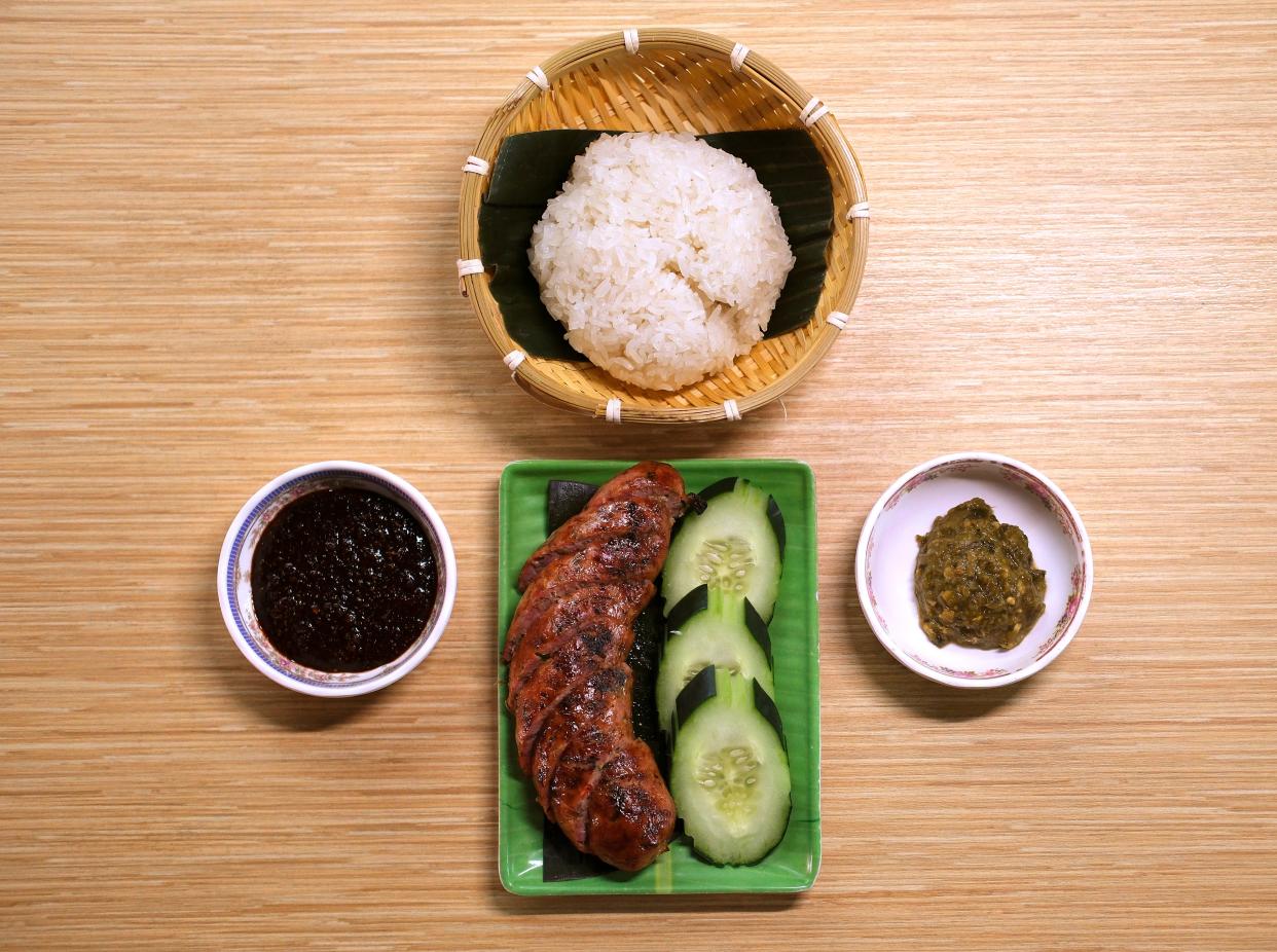 Sai Oua is a housemade savory and herbaceous Lao pork sausage, surrounded by Jaew Bong, roasted sweet chili dip, left, Jaew Muk Phet, charred green chili dip, and sticky rice top at Ma Der Lao Kitchen restaurant in the Plaza District.