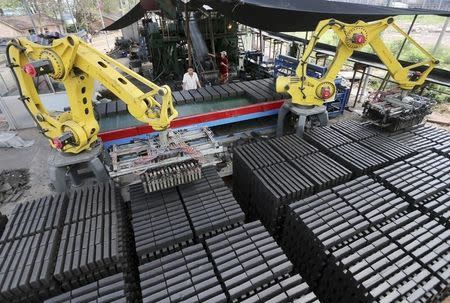 Workers look at machines moving newly made raw bricks at a factory in Huaibei, Anhui province July 31, 2014. REUTERS/China Daily
