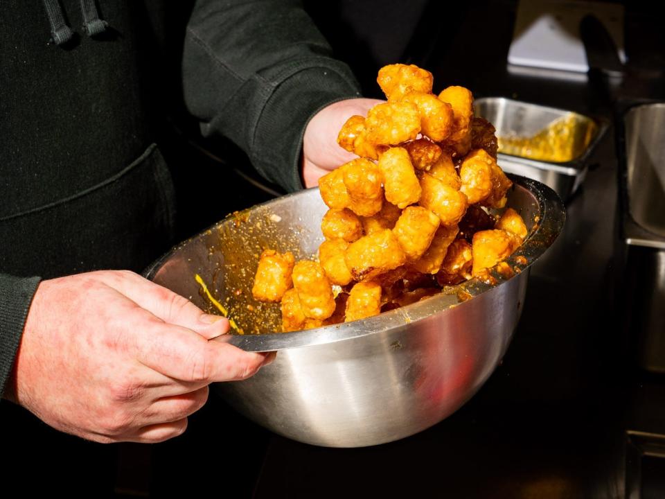 A chef tossing tater tots in a bowl.