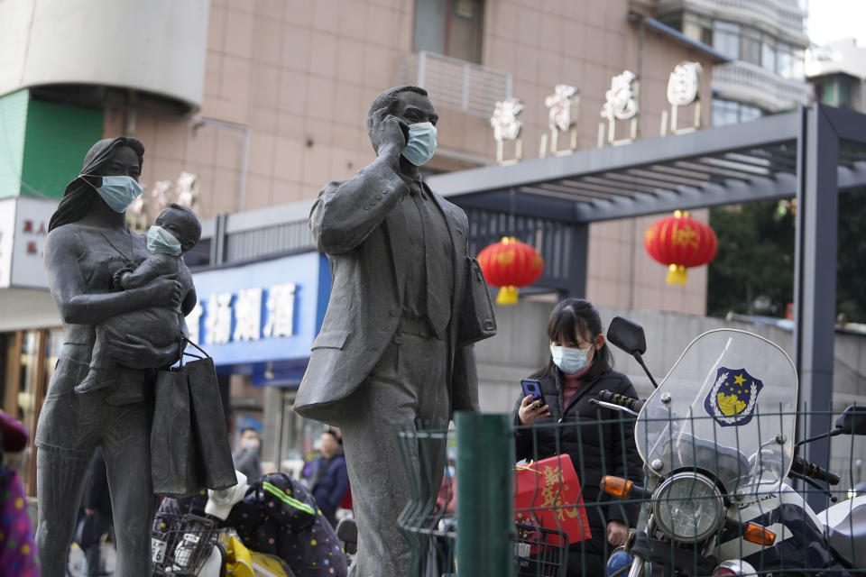 A woman wearing a mask walks past statues with masks placed on them in Wuhan in central China's Hubei province on Friday, Jan. 29, 2021. A World Health Organization team is visiting the central city of Wuhan where the coronavirus was first detected. (AP Photo/Ng Han Guan)