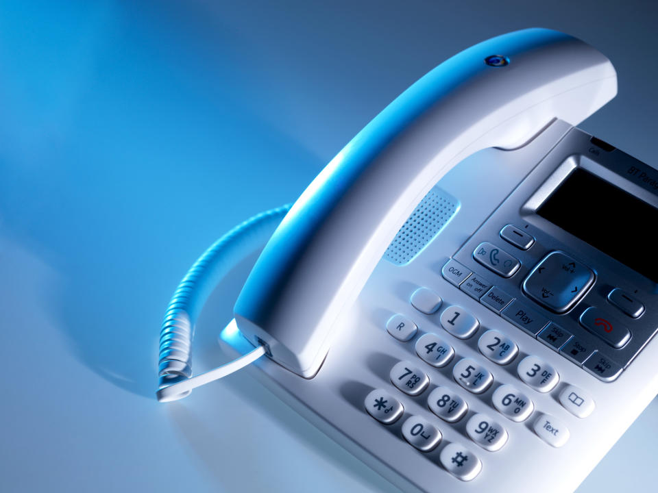 A close-up image of a white landline telephone with a corded handset resting on the base, featuring buttons and a small display screen