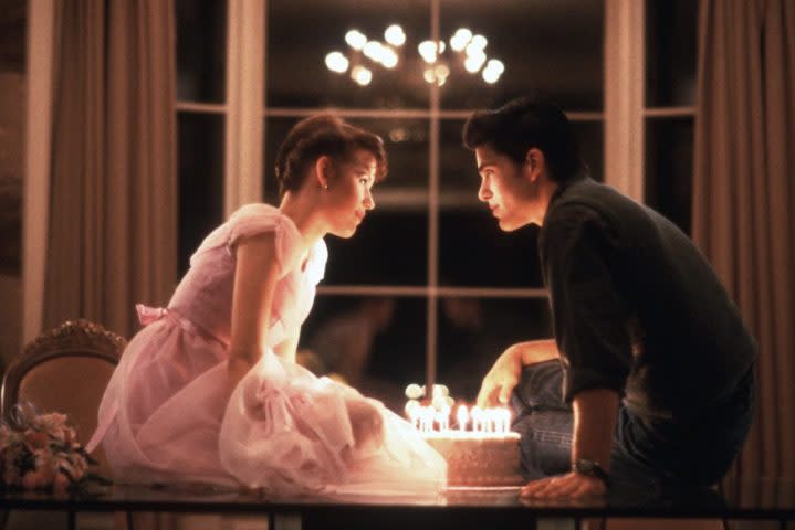 Molly Ringwald and Michael Schoeffling sit on a table and lean in over a birthday cake.