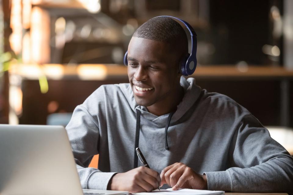 A smiling person wearing headphones and looking at a laptop computer.