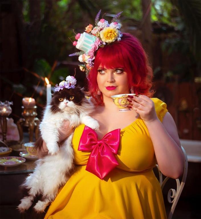 This cat mom dresses up with her cats, here she is drinking tea and wearing a floral head dress. Her cat is wearing one too.