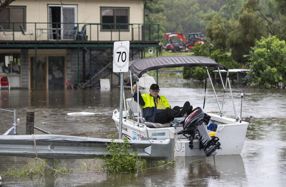 Resident Gary Evans waits in a boat for his family before returning to his house surrounded by flood waters at Londonderry on the outskirts of Sydney, Australia, Tuesday, March 23, 2021. Hundreds of people have been rescued from floodwaters that have isolated dozens of towns in Australia's most populous state of New South Wales and forced thousands to evacuate their homes as record rain continues to inundate the countries east coast. (AP Photo/Mark Baker)