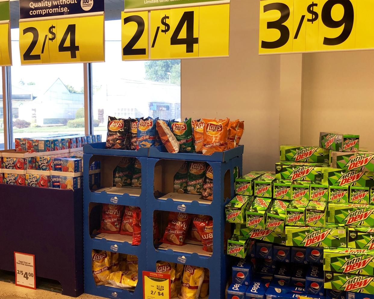 Brand-name section at Save A Lot Kool Aid, Lay's, and Pepsi products, on sale, against front with windows showing outside during summer