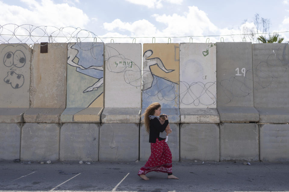 A woman holds a baby as she walks on an area at the Nitzana border crossing with Egypt, in southern Israel, Wednesday, Feb. 14, 2024, protesting against the humanitarian aid to enter Gaza until all the hostages are released. (AP Photo/Ohad Zwigenberg)