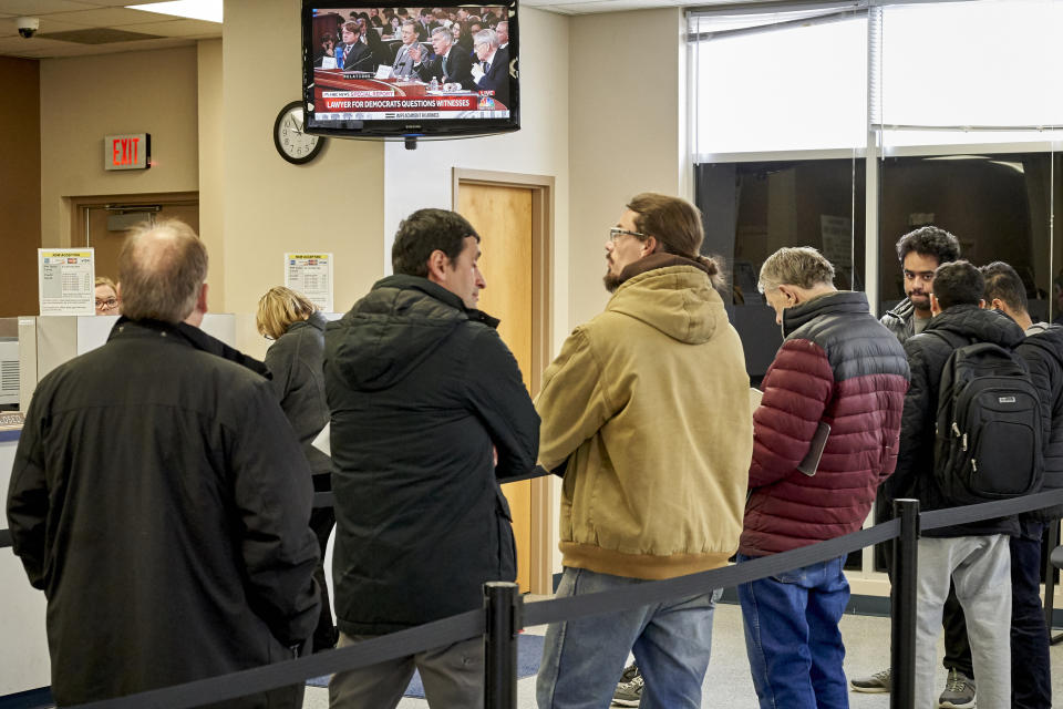 People wait in line at the Douglas County Treasurer's office in Omaha, Neb., Wednesday, Nov. 13, 2019, in front of a television broadcast of the public hearings in the impeachment inquiry against President Trump. (AP Photo/Nati Harnik)