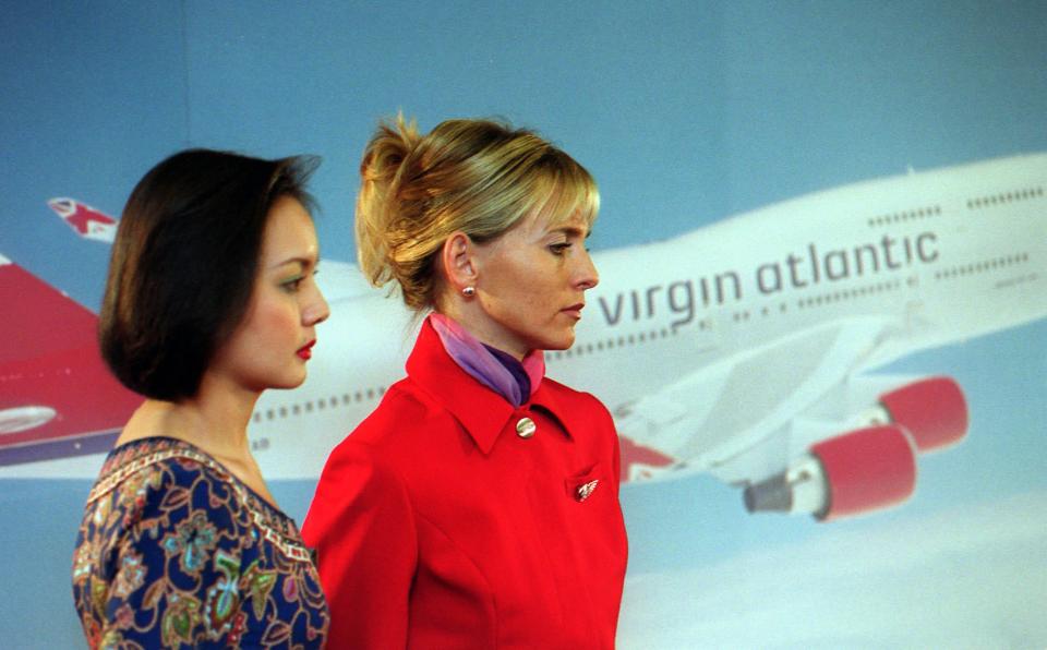 Flight Attendants for Virgin Atlantic (R) and Singapore Airlines pictured in 1999 at a press conference in London, in which Virgin Atlantic Chairman Richard Branson announced that SIA has signed a memorandum to acquire 49 percent of Virgin Atlantic.