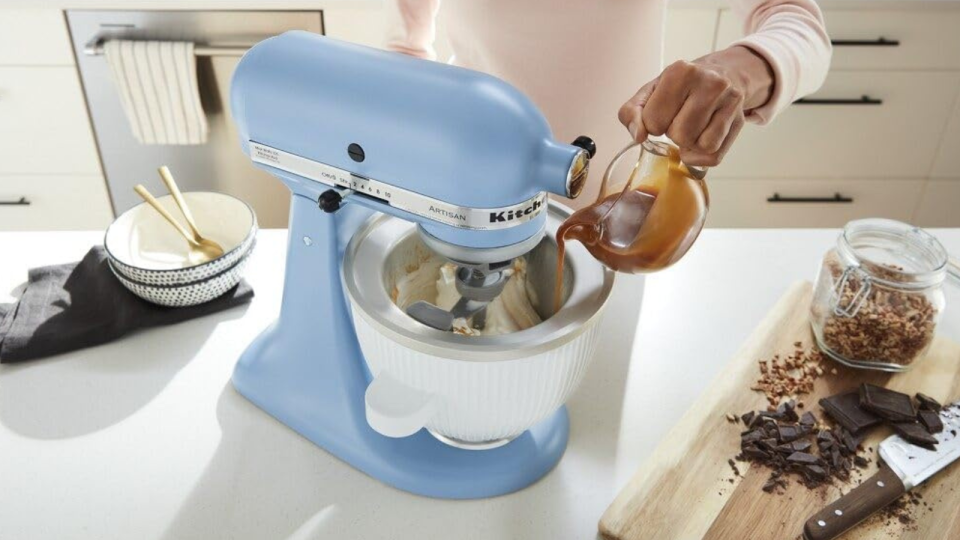 Someone pouring caramel sauce into the KitchenAid ice cream maker attachment, which is fixed to a KitchenAid stand mixer