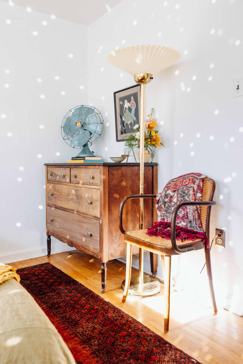 Corner view of white bedroom shows wood dresser and chair.