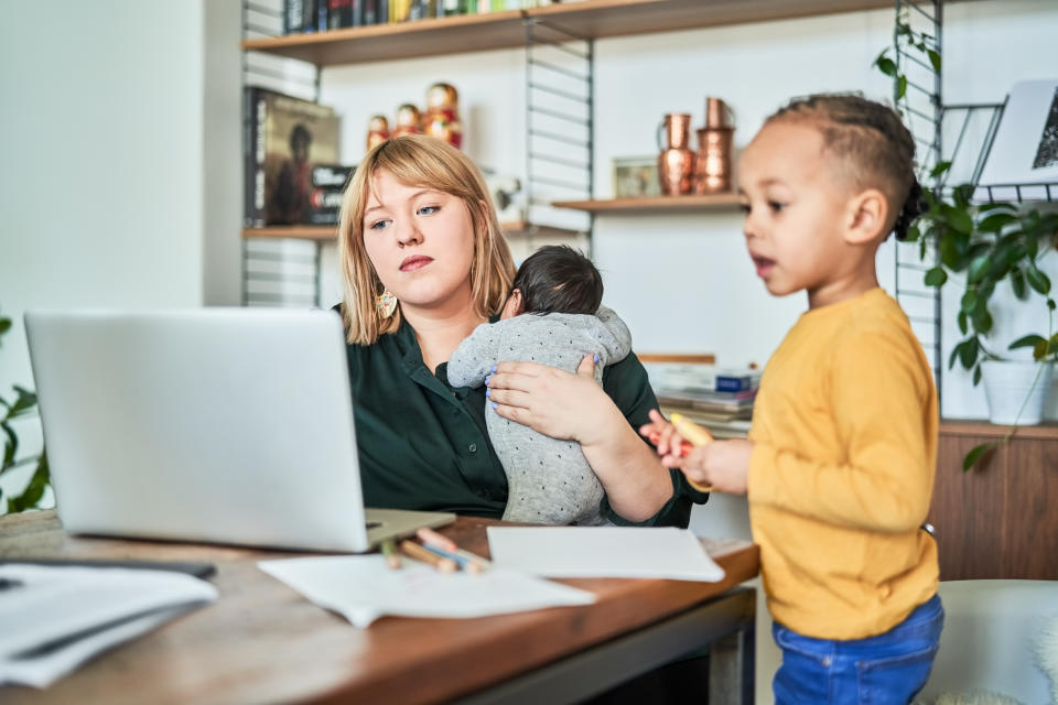 A single mother working from home with a newborn baby. A woman using her laptop while her son is playing in the living room.