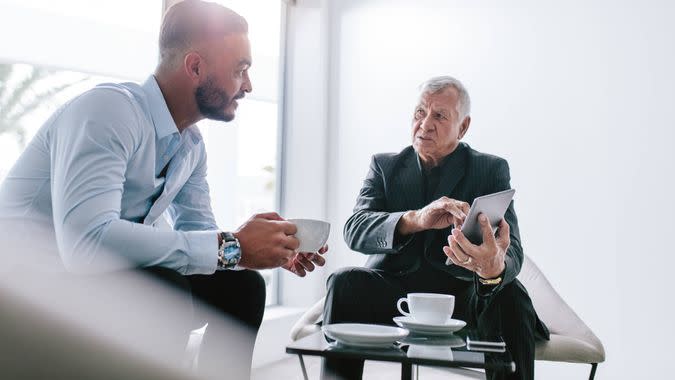 Two businessman sitting in office lobby discussing work over a cup of coffee.