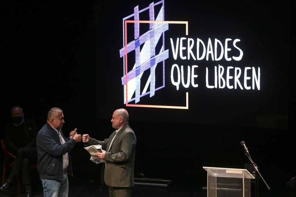 Armando Acuña, left, a former city councilman who was kidnapped by the Revolutionary Armed Forces of Colombia, FARC, hands former FARC commander Carlos Antonio Lozada, the bag Acuña was given by the rebels for his personal belongings while he was in captivity, during an event at the Truth Commission to commemorate victims of the country’s decades-long armed conflict, in Bogota, Colombia, Wednesday, June 23, 2021. (AP Photo/Ivan Valencia)