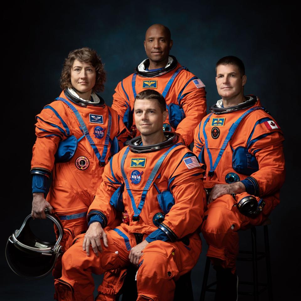 four astronauts in orange spacesuits pose for portrait