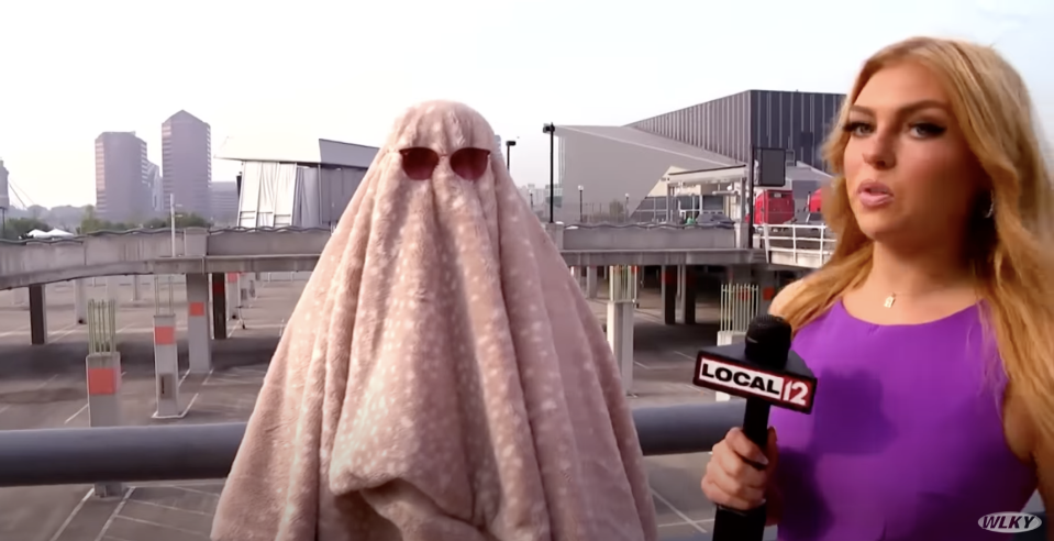 Reporter interviewing a person wearing a "Cousin It"–type outfit, with a blanket over their head, and sunglasses