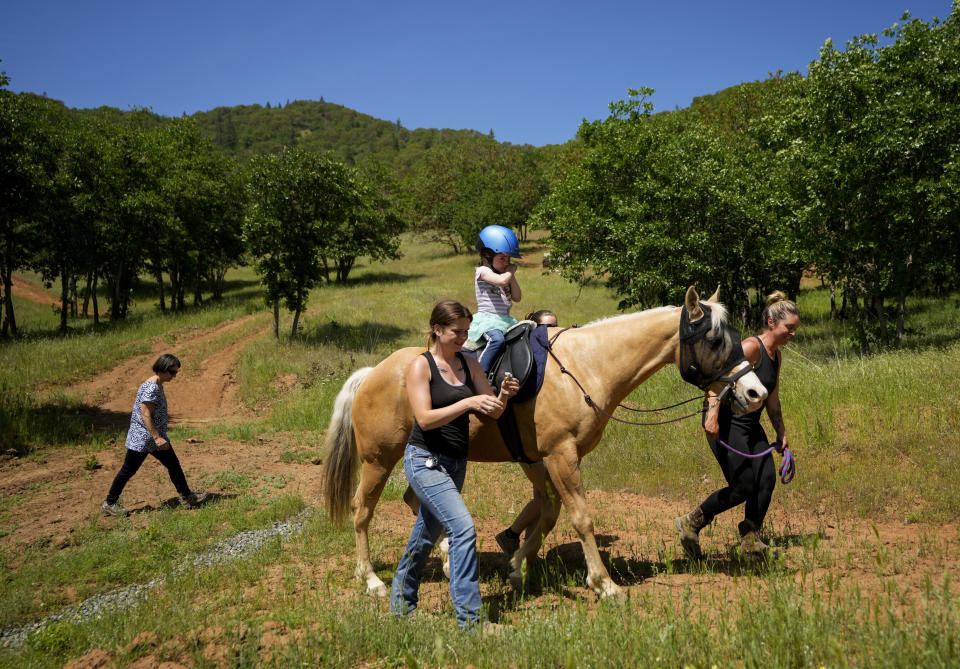 Jessi Hendrickson, left, and Hollie Tenberge, right, work with Scarlett Rasmussen, 8, to ride horse Callie at the Foundation of Southern Oregon, May 17, 2023, in Rogue River, Ore. Chelsea Rasmussen fought for more than a year for her daughter, Scarlett, to attend full days at Parkside and says school employees told her the district lacked the staff to tend to Scarlett’s medical and educational needs, which the district denies. (AP Photo/Lindsey Wasson)