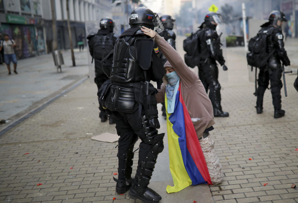 An anti-government protester kneels before a police officer in Bogota, Colombia, Friday, Nov. 22, 2019. Labor unions and student leaders called on Colombians to bang pots and pans on Friday evening in another act of protest while authorities announced three people had died in overnight clashes with police after demonstrations during a nationwide strike. (AP Photo/Ivan Valencia)