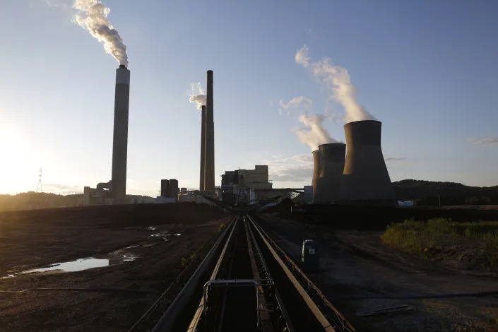 Outdoor conveyor belt that leads to massive smoke stacks with smoke billowing from them.