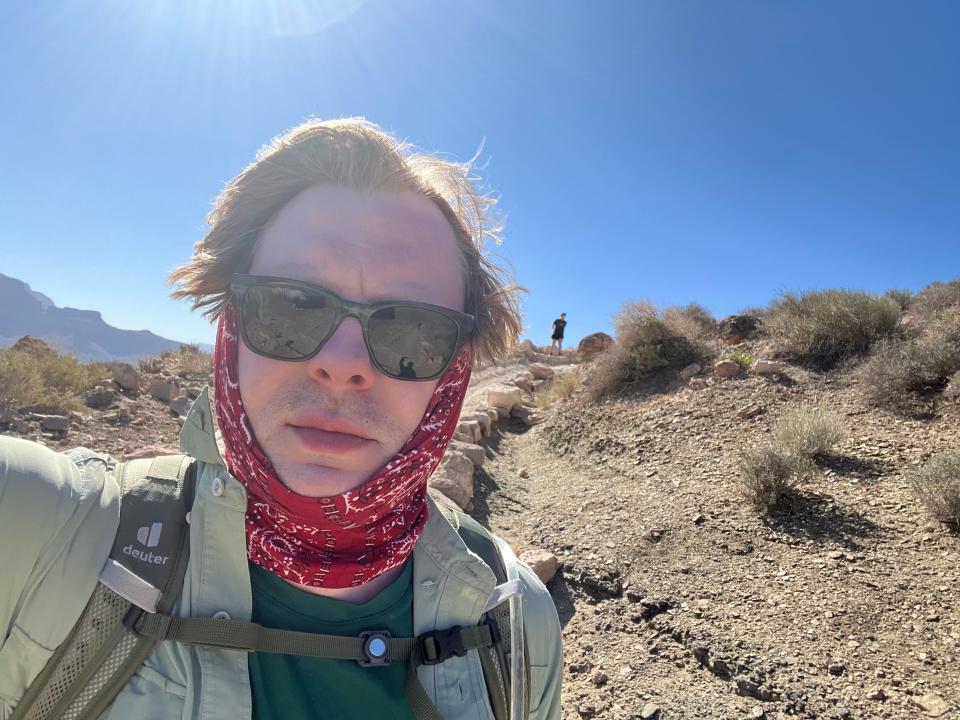 A man taking a selfie with a scarf wrapped around his neck, wearing sunglasses.