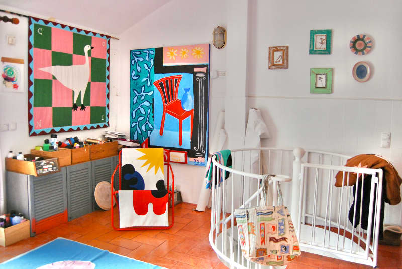 Paint in boxes above gray cabinets in white room with colorful tapestries and artwork at top of spiral staircase.