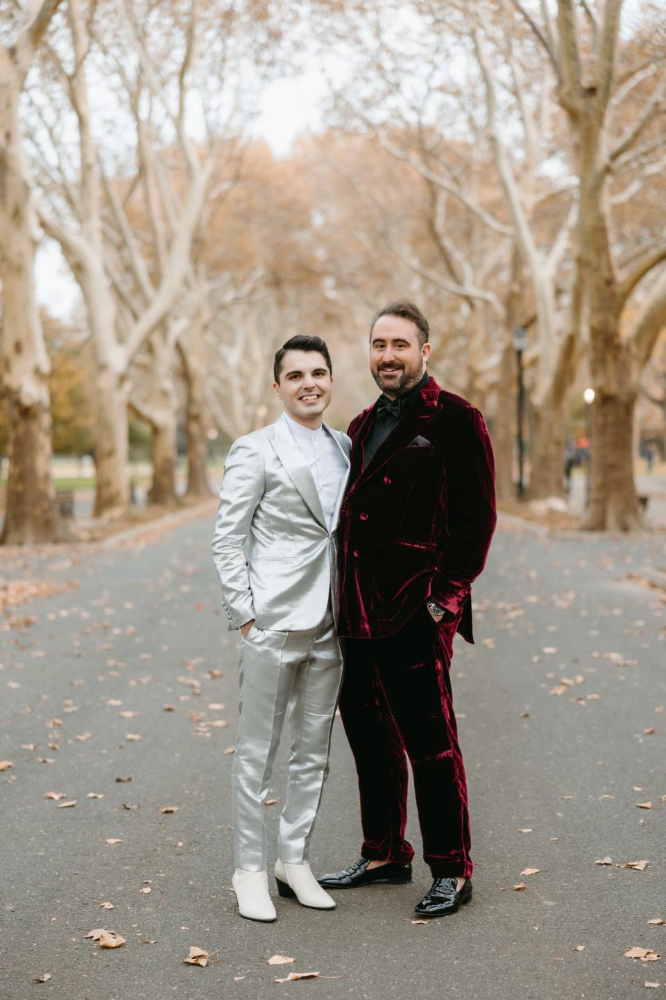 Two men in colorful suits stand in a park, embracing.