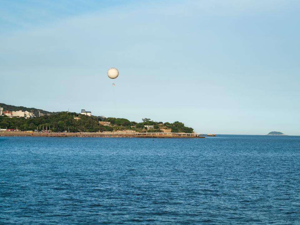 A photograph of a weather balloon hovering over a distant shoreline.