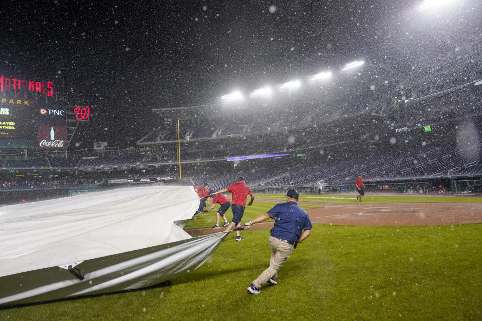 The grounds crew covers the field with a tarp during a rail delay in the seventh inning of a baseball game between the Washington Nationals and the Colorado Rockies at Nationals Park, Tuesday, July 25, 2023, in Washington. (AP Photo/Alex Brandon)