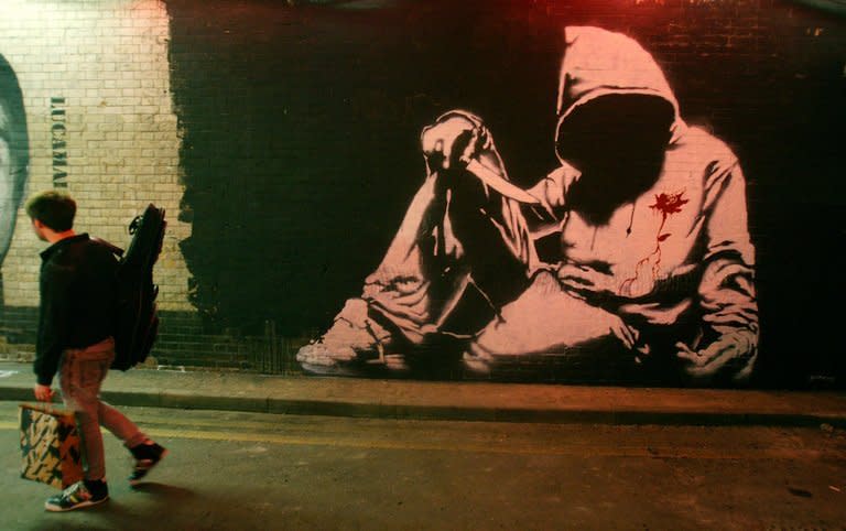 A man walks past a Banksy graffiti artwork during "Cans" graffiti exhibition in London on May 3, 2008. Far from London's beaten tourist track, a group of visitors is staring keenly at the graffiti-covered gates to an abandoned construction site